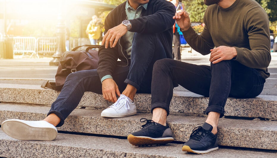 Lifestyle photo of two male friends sitting on the steps in city street and talking wearing casual street style clothes and sneakers.