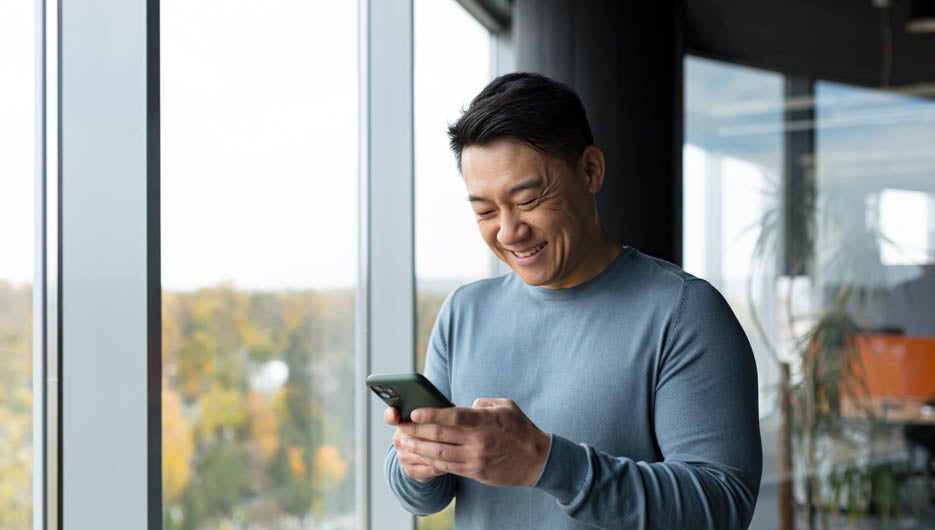 Successful and happy Asian man uses the phone online in the offi