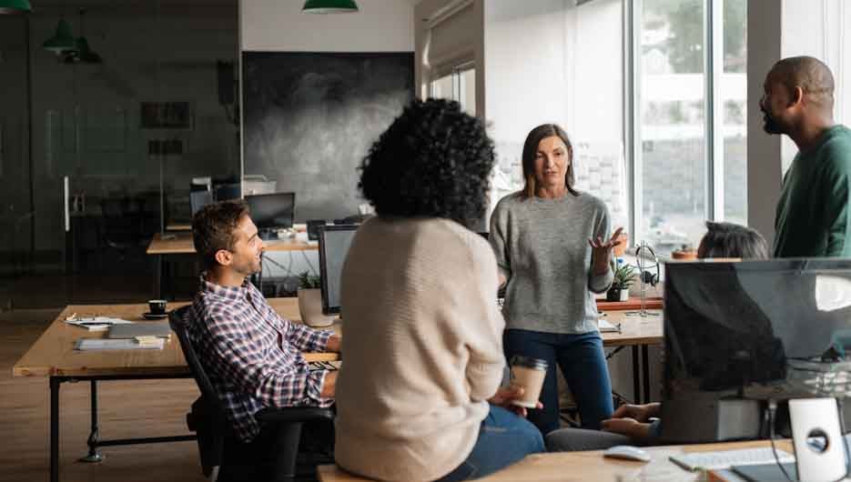 Smiling group of diverse designers discussing business together while having a casual meeting around their desks in their startup office
